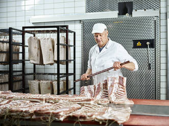 Metzger mit Mütze beim Anrichten von rohem Fleisch in einer Fabrik - CVF01863
