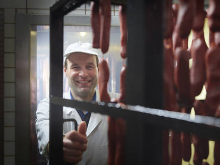 Glücklicher Fleischer bei der Arbeit in der Räucherkammer einer Fabrik - CVF01871