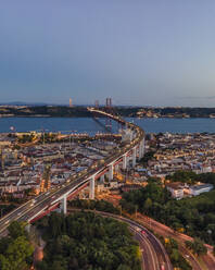 Luftaufnahme der Brücke des 25. April mit der Christkönigsstatue (Cristo Rei) im Hintergrund bei Sonnenuntergang, Blick auf die Skyline von Lissabon bei Nacht, Alcântara, Lissabon, Portugal. - AAEF14026