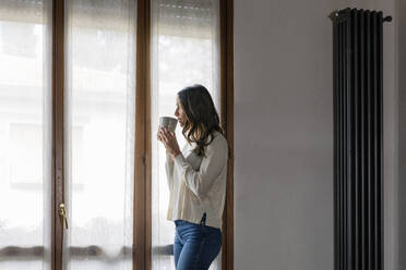 Nachdenkliche Frau trinkt Kaffee am Fenster - EIF03196
