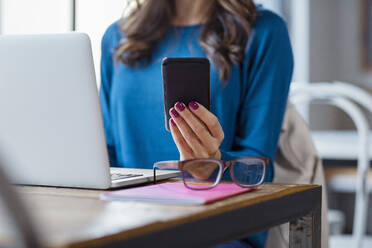 Freelancer using smart phone by eyeglasses on table in cafe - EIF03201