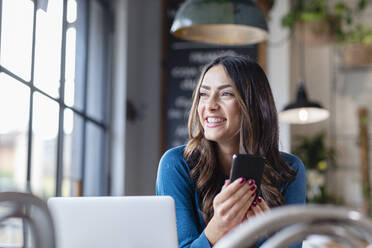 Glückliche Geschäftsfrau mit Laptop und Smartphone in einem Café - EIF03206