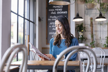 Lächelnde junge Frau, die in einem beleuchteten Cafe ein Buch liest - EIF03208
