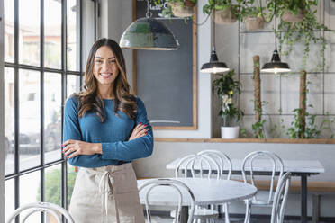 Smiling woman standing with arms crossed in cafe - EIF03221