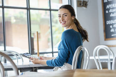 Lächelnder Unternehmer mit Taschenrechner am Tisch in einem Kaffeehaus - EIF03224