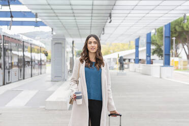 Nachdenkliche Geschäftsfrau mit Einweg-Kaffeebecher an der Straßenbahnhaltestelle - EIF03232