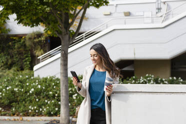 Young woman with disposable coffee cup using smart phone in city - EIF03242