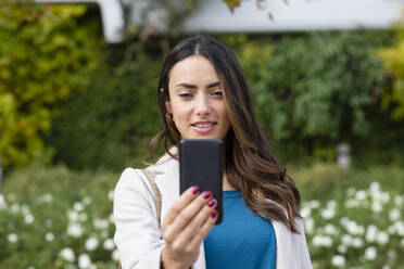 Junge Geschäftsfrau benutzt Mobiltelefon im Park - EIF03250