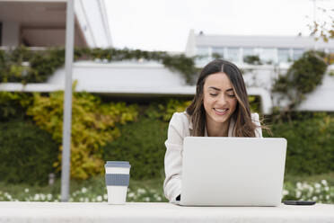 Smiling businesswoman working on laptop in park - EIF03258