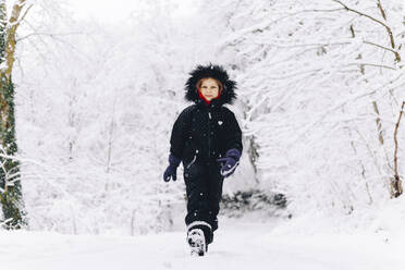 Lächelndes Mädchen, das auf schneebedecktem Boden im Winterwald spazieren geht - OMIF00514
