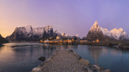 Stone quay located on calm sea water near Reine village and snowy mountain ridge against sundown sky on Lofoten Islands, Norway - ADSF33532