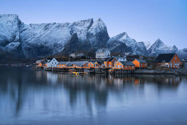Häuser des Dorfes Reine am Meeresufer vor gefrorenen Bergen und bedecktem Himmel im Winter auf den Lofoten, Norwegen - ADSF33535