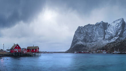 Häuser des Dorfes Reine am Meeresufer vor gefrorenen Bergen und bedecktem Himmel im Winter auf den Lofoten, Norwegen - ADSF33537