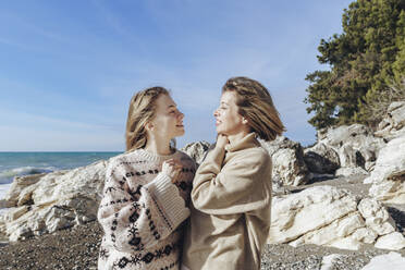 Woman with daughter wearing sweater at beach on sunny day - OMIF00518