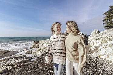 Tochter mit Mutter spazieren am Strand an einem sonnigen Tag - OMIF00521