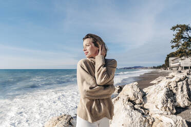 Frau mit Hand im Haar am Strand stehend - OMIF00530