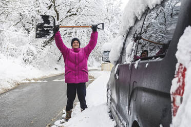 Lächelnder Mann mit Schaufel am Auto im Winter - OMIF00533