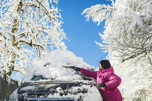 Mann mit Strickmütze räumt Schnee mit Schaufel auf Auto - OMIF00541