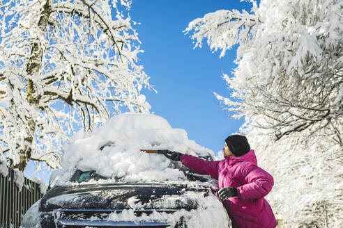 Mann mit Strickmütze räumt Schnee mit Schaufel auf Auto - OMIF00541