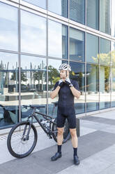 Junger Mann mit Fahrradhelm auf dem Fahrrad vor einem Bürogebäude - IFRF01500