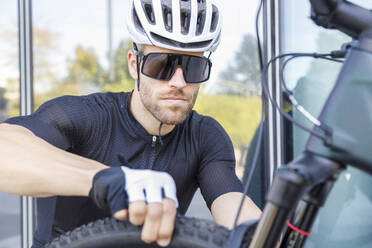 Junger Mann mit Sonnenbrille und Helm bei der Reifenkontrolle - IFRF01512