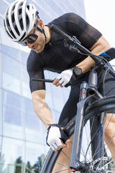 Young man wearing sunglasses and helmet examining tire - IFRF01521