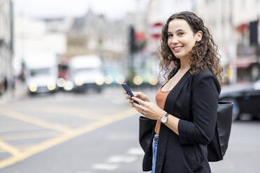 Smiling businesswoman with smart phone in city - WPEF05744