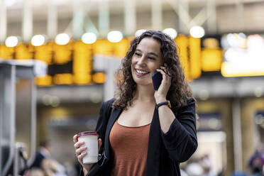 Lächelnde Frau mit Einweg-Kaffeebecher im Gespräch mit einem Smartphone - WPEF05749