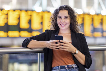 Lächelnde junge Frau mit Smartphone am Bahnhof - WPEF05752
