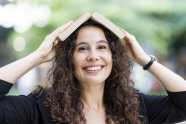 Smiling woman holding open book on head - WPEF05754
