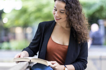 Lächelnde Frau, die auf einer Bank ein Buch liest - WPEF05756