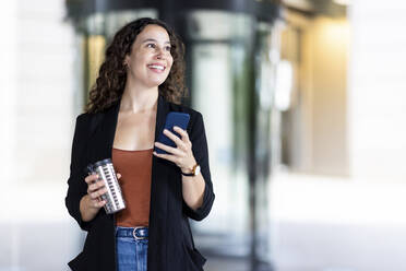 Smiling businesswoman with reusable cup and smart phone - WPEF05757