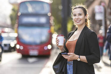 Lächelnde Geschäftsfrau mit Einweg-Kaffeebecher auf der Straße in der Stadt - WPEF05767