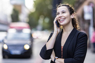 Geschäftsfrau lachend und am Smartphone sprechend in der Stadt - WPEF05775