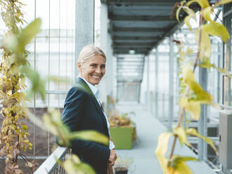 Happy agronomist standing in corridor at plant nursery - JOSEF06655