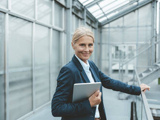 Smiling businesswoman with tablet PC in office corridor - JOSEF06674
