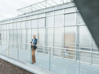 Contemplative businesswoman standing on balcony at office - JOSEF06675