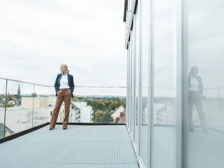 Kontemplative Geschäftsfrau vor klarem Himmel auf dem Balkon eines Büros stehend - JOSEF06677