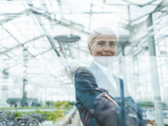 Scientist with arms crossed seen through glass of plant nursery - JOSEF06679