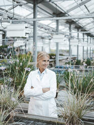 Contemplative scientist with arms crossed in plant nursery - JOSEF06692