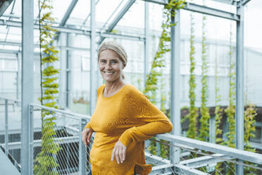 Smiling scientist leaning on railing at plant nursery - JOSEF06719