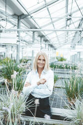 Smiling agronomist standing amidst plants at garden center - JOSEF06736