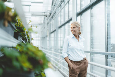 Smiling agronomist with hands in pockets at greenhouse - JOSEF06759