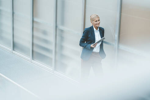 Contemplative businesswoman with tablet PC in office corridor - JOSEF06779