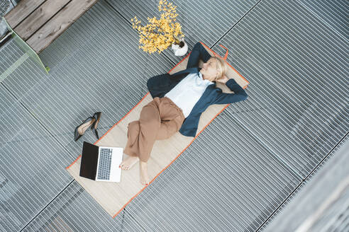 Businesswoman with hands behind head resting on desk at office - JOSEF06787