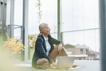 Contemplative businesswoman with laptop sitting in office - JOSEF06788