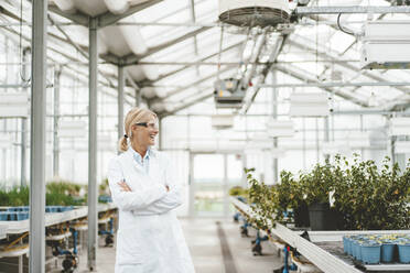 Cheerful scientist with arms crossed in plant nursery - JOSEF06796