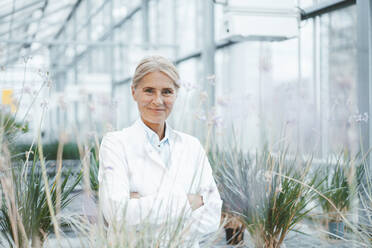 Smiling biologist with arms crossed in greenhouse - JOSEF06797