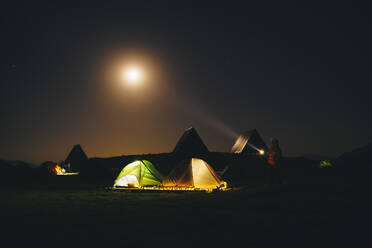 Tourist with flashlight standing near illuminated tents at Caucasian State Nature Reserve in Sochi, Russia - OMIF00543