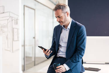 Geschäftsmann mit Tasse und Smartphone auf dem Schreibtisch im Büro - JOSEF06842